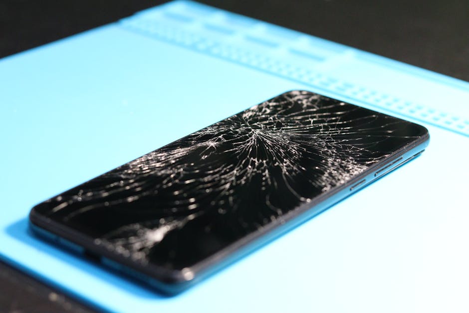 A cracked smartphone screen on a repair mat highlights technology mishaps.
